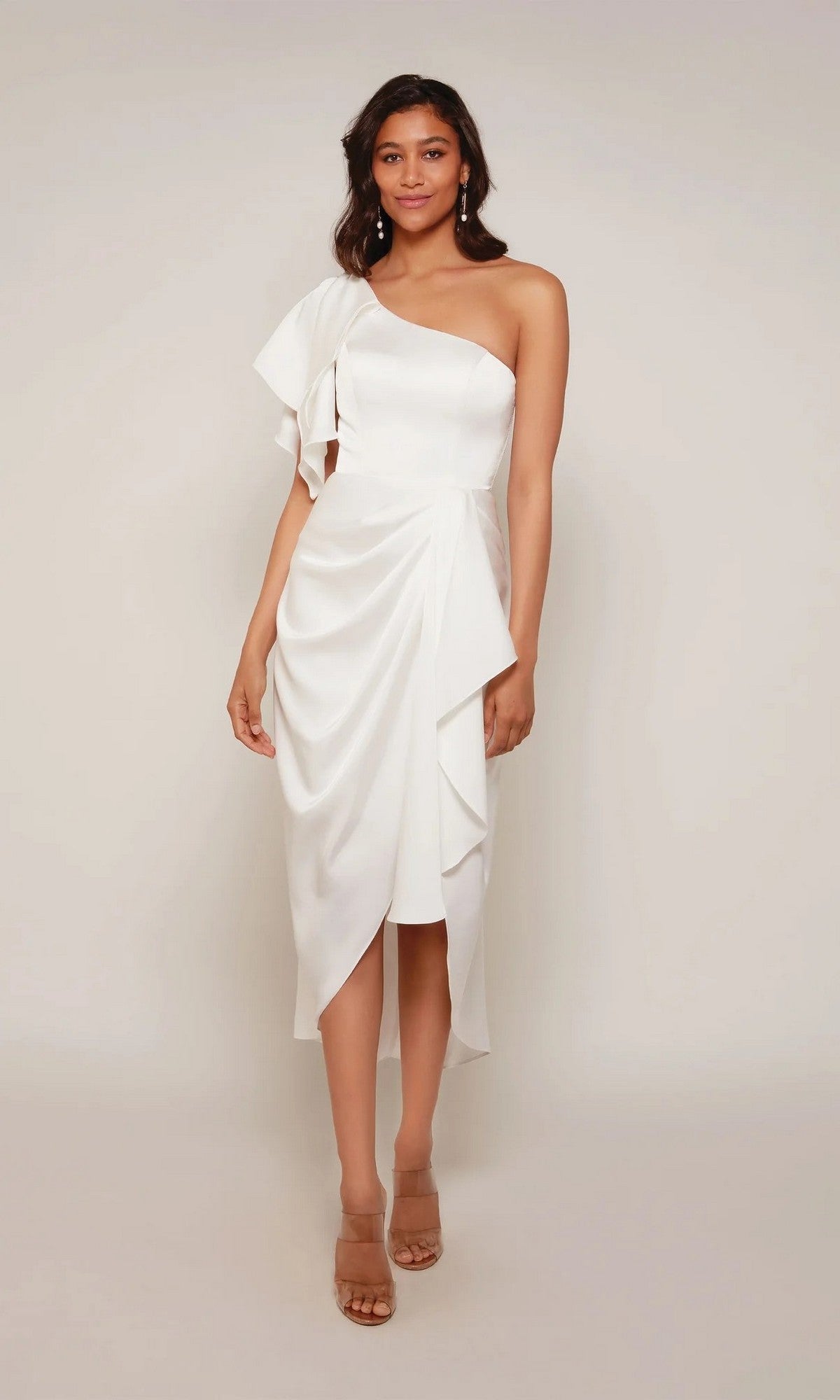 A woman wears the Alyce 70035 knee-length semi-formal dress in diamond white, featuring a one-shoulder design with draped details and nude heeled sandals against a plain background.